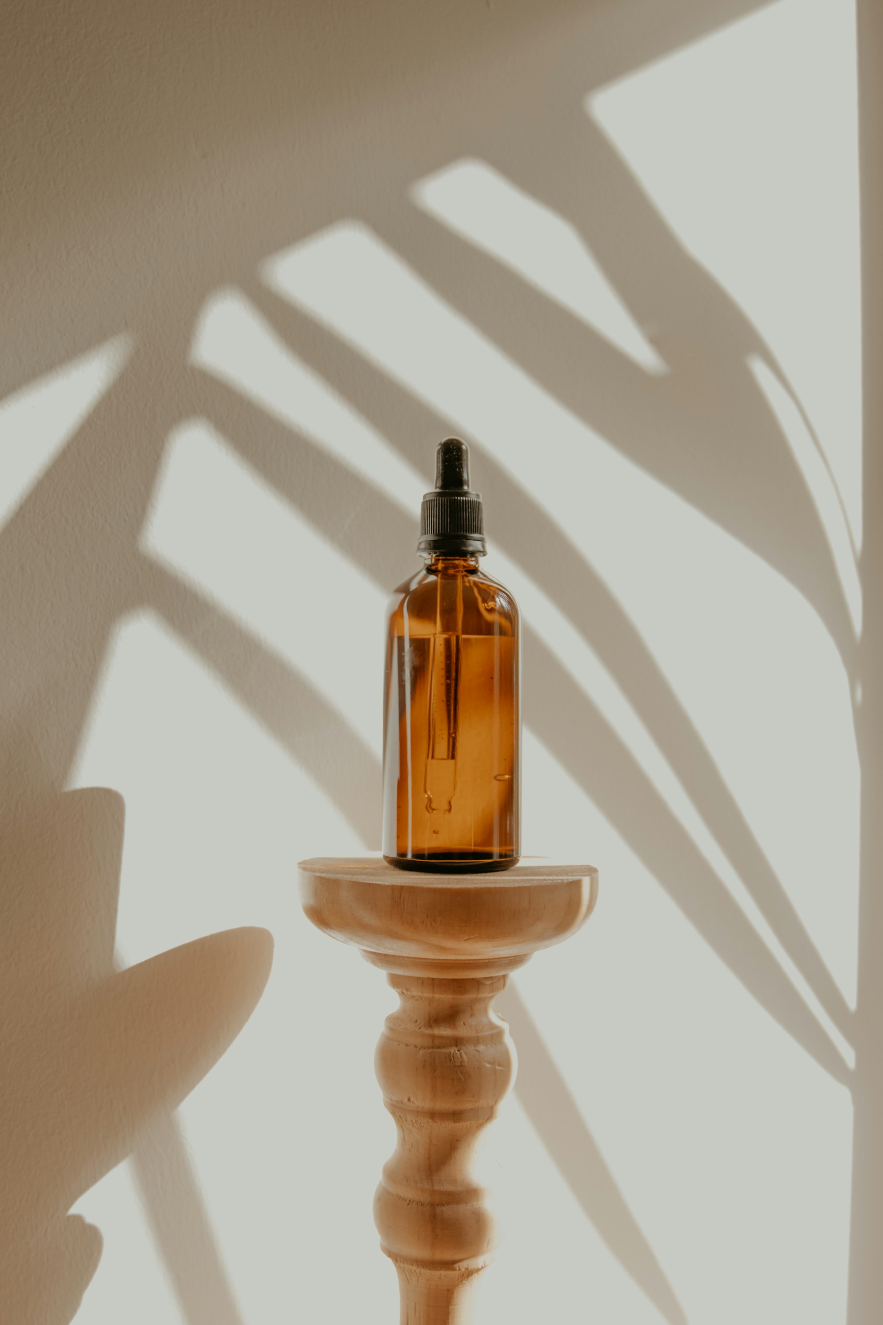 An amber glass bottle on a wooden stand in soft botanical shadows